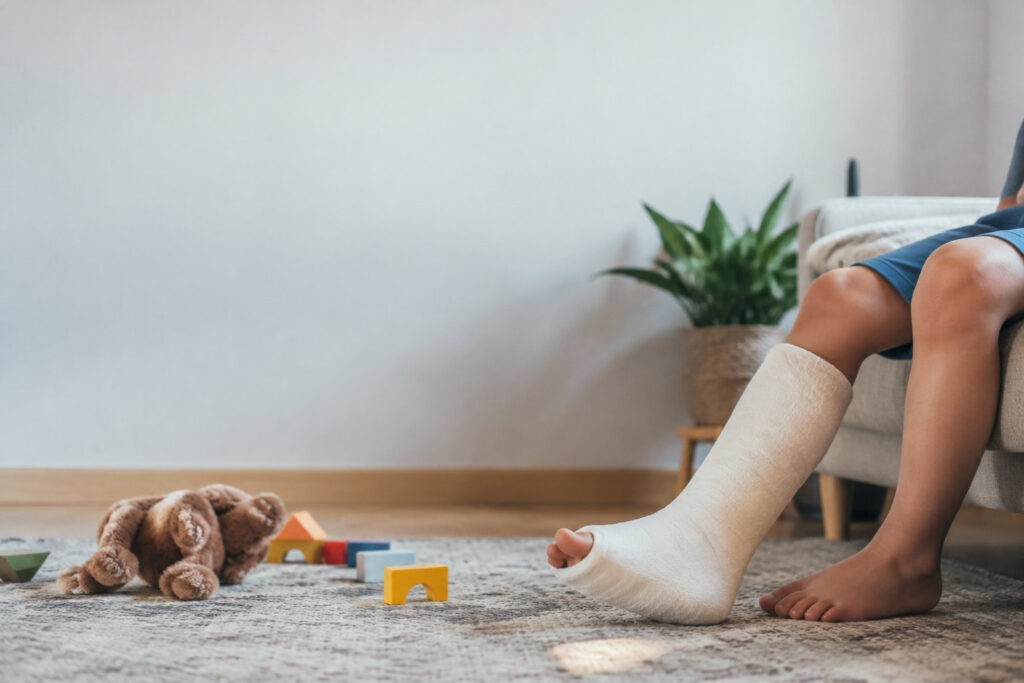 Un enfant assis sur un canapé avec le tibia plâtré après une fracture en motte de beurre, entouré de jouets.